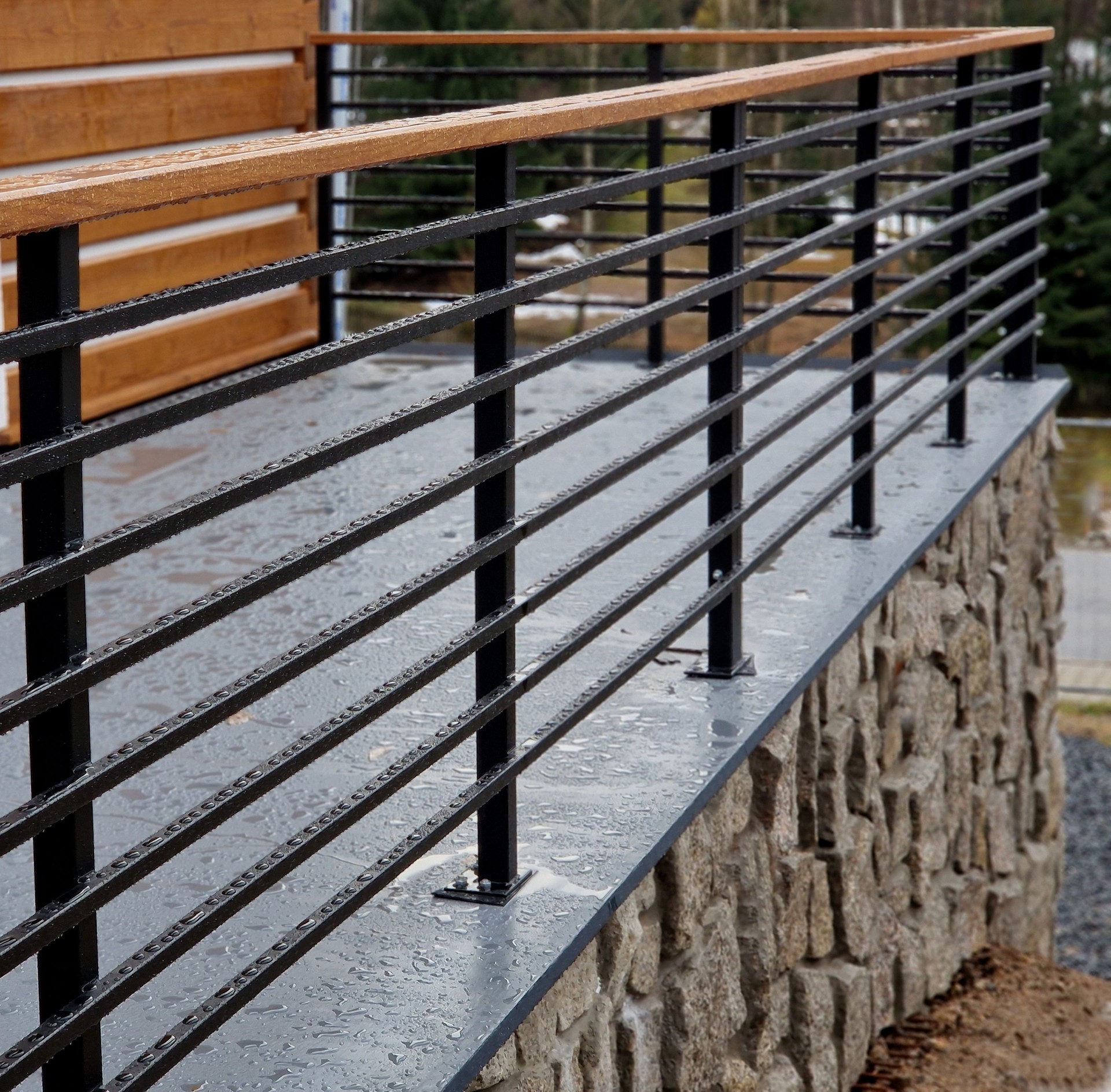 black railing with metal longitudinal section and handle made of wood. wet and new on the terrace at the cottage. the locksmith attached the bolts to the ground. blacksmith work advertisement